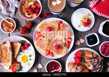 Valentines or Mothers Day brunch table scene. Top view on a dark wood background. Heart shaped pancakes, eggs and an assortment of love themed food. Stock Photo