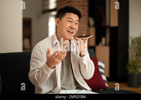 Portrait of happy asian man holding cellphone near mouth and recording message, using digital assistance app Stock Photo
