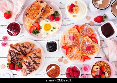 Valentines or Mothers Day brunch table scene. Overhead view on a white wood background. Heart shaped pancakes, eggs and assorted love themed food. Stock Photo