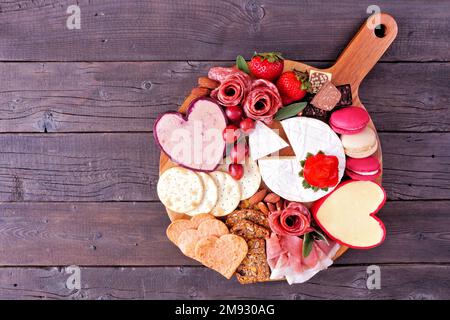 Valentine's Day theme charcuterie board with a selection of cheeses, appetizers and sweets. Overhead view on a dark wood background. Stock Photo