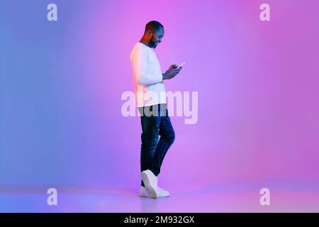 Cheerful black man using cell phone, studio shot, side view Stock Photo
