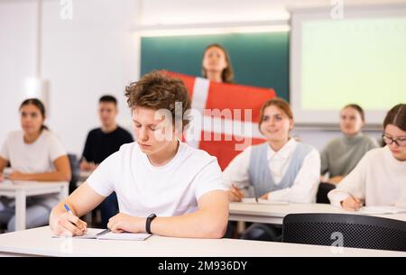 High school teacher tells students about Denmark and holds a Denmark flag in hands. Stock Photo