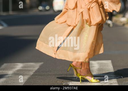 Milan, Italy - February 25, 2022: Unrecognizable female in stylish pink dress and high heeled sandals walking on crosswalk on sunny day on city street Stock Photo