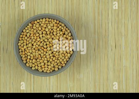Soybeans in bowl on a straw background. Protein pulse that is dried and then soaked and cooked before eating. Vegetarian product. Top view. Stock Photo