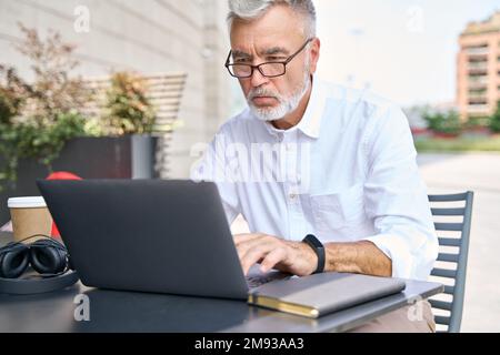Focused older business man using computer working online outdoor. Stock Photo