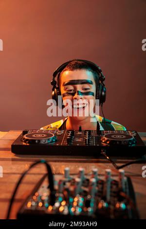 Young performer looking at dj turntables in studio, preparing to mix techno music and have fun at nightclub. Woman with crazy make up watching mixer on table, look closely and acting silly. Stock Photo