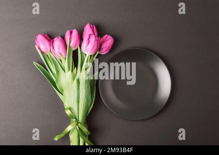 Black plate and purple tulips on black background. Top view, flat lay, mockup. Stock Photo