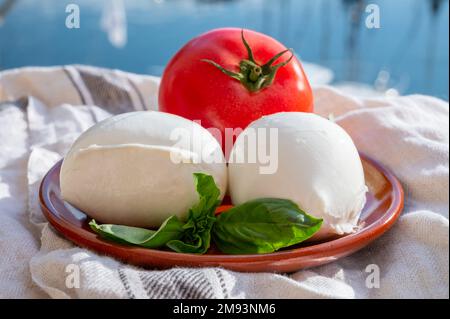 White soft italian mozzarella bufala cheese in balls with red tomato and basil served outdoor Stock Photo