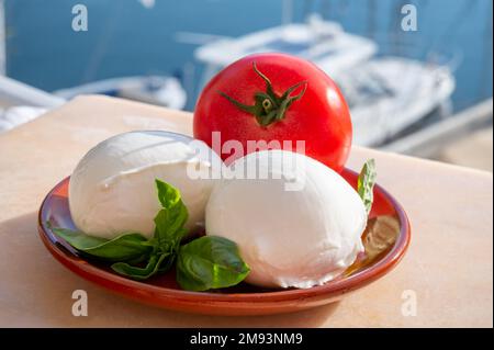 White soft italian mozzarella bufala cheese in balls with red tomato and basil served outdoor Stock Photo