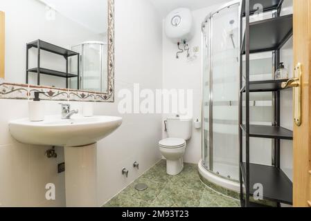 Bathroom with white porcelain one-piece pedestal sink and valance-framed wall mirror, corner shower stall and black metal shelving Stock Photo