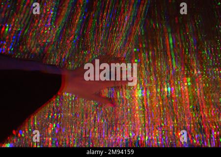 Glitch image hands with a beautiful ring a dancing bizarre woman in background of a copper-plated metal Sequins Tinsel curtain shining neon lighting Stock Photo