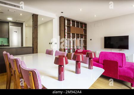 Living room with various furniture, open kitchen, metal pillars and decorative details in purple Stock Photo