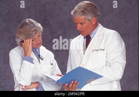 Older male doctor looking at medical records and discussing with female doctor Stock Photo