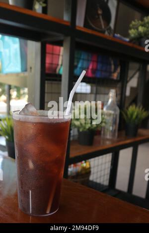 sweet iced tea with a straw in a plastic cup on a background of potted plants Stock Photo
