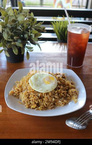 special fried rice with fried egg served on a white plate against a glass of iced tea in the background Stock Photo