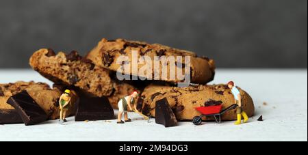 Three miniature farmers dragging chocolate chip cookies and cart. Miniature people and chocolate cookies with business concept. Stock Photo