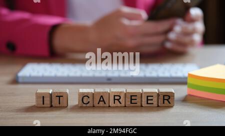IT specialist working on keyboard at office desk, wooden cubes with words IT career in front of him. Stock Photo