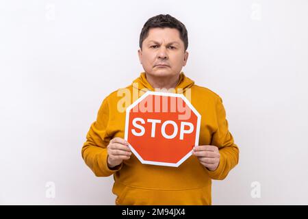 Portrait of middle aged serious self confident holding stop sign, warning to follow to traffic rules, wearing urban style hoodie. Indoor studio shot isolated on white background. Stock Photo