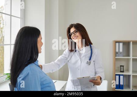 Cheerful female doctor holding patient by her shoulder giving support Stock Photo