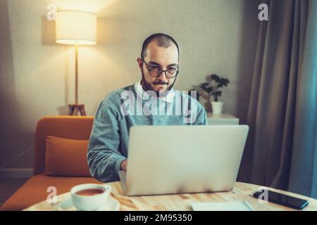 Male freelancer or IT code developer working at laptop. Programmer or young businessman at home office, distant job. Stock Photo