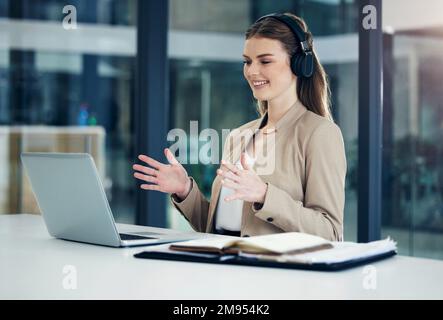 Sharing her big ideas with others. a young businesswoman wearing headphones while having a video call on a laptop in an office. Stock Photo