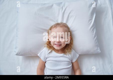 Top view head curly-haired girl's child lying bed white sheet, pillow. Mockup for the image of deer antlers. The concept of good mood and New Year Stock Photo