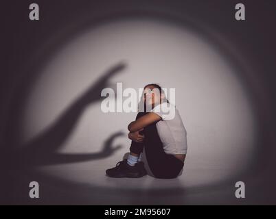 Every day begins with an act of courage and hope. a young woman sitting in a dark room with a scary figure on the wall. Stock Photo