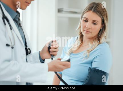 .a doctor using a blood pressure gauge during a checkup with his pregnant patient. Stock Photo