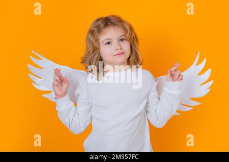 Child angel crossed fingers with lucky and hope, good luck. Valentines day. Little cupid angel child with wings. Studio portrait of angelic kid. Stock Photo