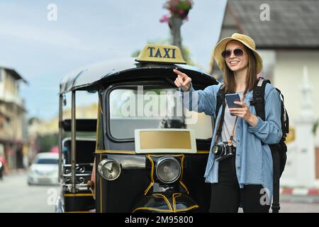 Happy caucasian female traveller with backpack using smart phone front of Tuk Tuk taxi in Chiang Mai Northern Thailand Stock Photo