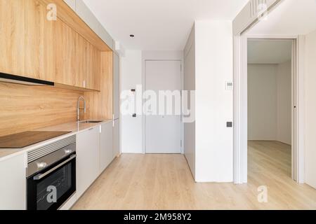 Simple small modular kitchen area along the wall in studio apartment next to front door and doorway to an empty bedroom. Furniture minimalism with Stock Photo