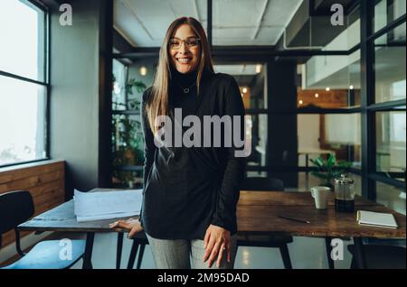 Successful female entrepreneur smiling at the camera while standing in an office. Happy young businesswoman standing in the boardroom of a modern work Stock Photo