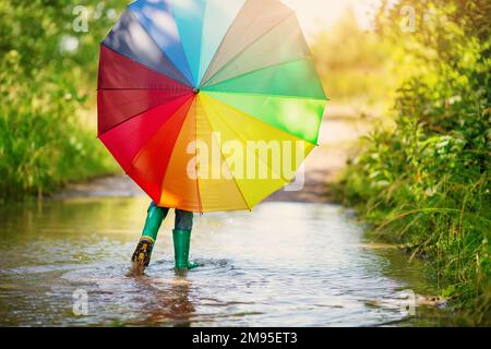 Boy walking through the puddle with colorful umbrella in his hands. Stock Photo