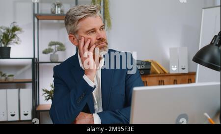 Stressed sad mature businessman losing job having financial problems at office workplace. Frustrated middle aged gray-haired freelancer man thinking of money debt, budget loss bankruptcy. Overworking Stock Photo