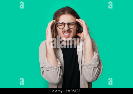 Young caucasian man in eyeglasses with headache rubbing his temples isolated over green background Stock Photo