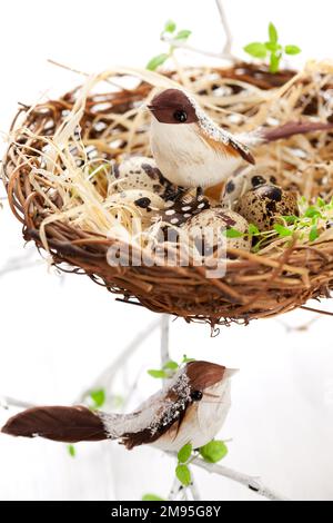 Decorative small birds, quail's eggs and birds feathers in an Easter nest. Easter composition for spring holiday. Stock Photo