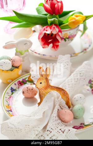 Easter table setting with treats sweet chocolate Easter eggs on plate, napkin, bunny and spring flowers and festive decorations. Stock Photo