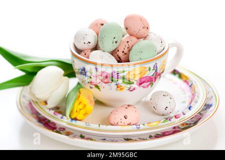 Easter treats sweet chocolate Easter eggs in bowl on plate around spring flowers and festive decorations. Easter table setting. Stock Photo