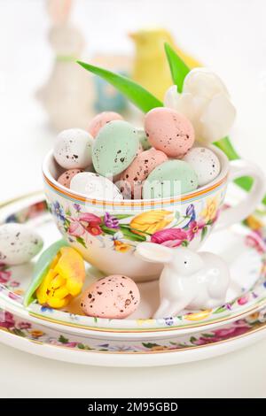 Easter treats sweet chocolate Easter eggs in bowl on plate around spring flowers and festive decorations. Easter table setting. Stock Photo