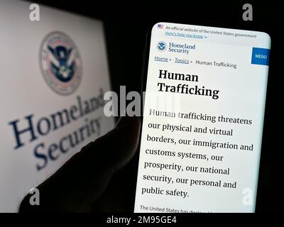Person holding cellphone with webpage of US Department of Homeland Security (DHS) on screen in front of seal. Focus on center of phone display. Stock Photo