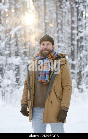 Portrait of young happy man smiling at camera while walking in the forest in winter Stock Photo