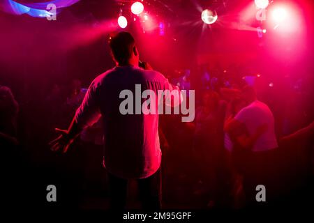 silhouette of the presenter with the microphone in hand on stage at a concert in a nightclub with a red background Stock Photo