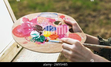 Palette with paints in the hands of an artist painting on the street, close-up Stock Photo