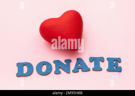 Red toy heart and inscription of wooden letters on a pink paper background, a concept on the theme of donation Stock Photo