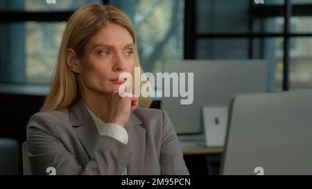 Thoughtful concerned Caucasian middle-aged adult 40s woman working on laptop computer in office looking away thinking solving problem. Serious pensive Stock Photo