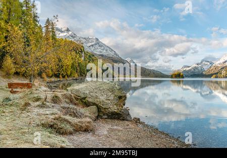 Park bench in a Autumn landscape at Lake Sils, Engadine, Switzerland with Piz Margna in the background Stock Photo