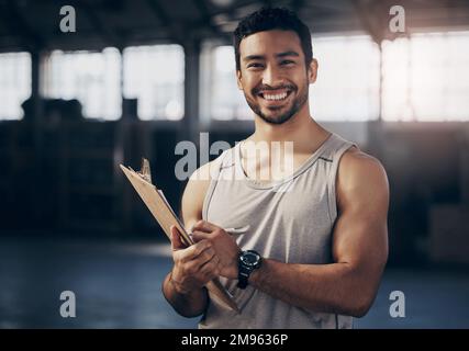 Ill help you fill out a membership form. Portrait of a muscular young man writing notes on a clipboard while working in a gym. Stock Photo