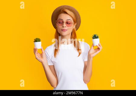 Woman holding a small cactus in hands gently on yellow background. Stock Photo