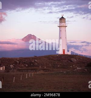 Cape Egmont lighthouse, with Mount Egmont (Mount Taranaki) in the background, on the west coast of North Island, New Zealand.  The lighthouse was erected here in 1877, and became fully automated in 1986. Stock Photo