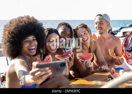 Happy multiracial friends making selfie while eating watermelon at boat party, young people having fun in sea tour, travel and luxury vacation concept Stock Photo